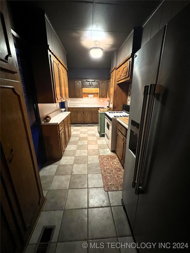 kitchen featuring white range with gas stovetop, visible vents, brown cabinetry, stainless steel fridge with ice dispenser, and light countertops