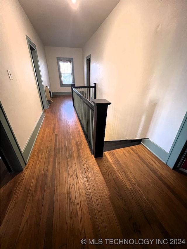 corridor featuring dark wood-style floors, an upstairs landing, and baseboards