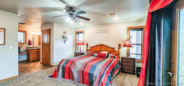 bedroom with ceiling fan, ensuite bathroom, a textured ceiling, and light carpet