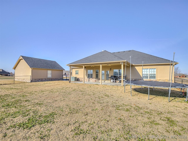 rear view of property with ceiling fan, a patio area, a trampoline, and a yard