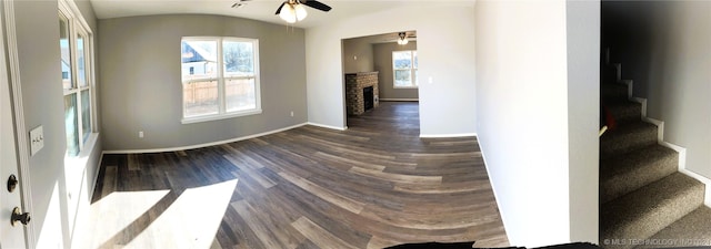 empty room with a brick fireplace, ceiling fan, and dark wood-type flooring