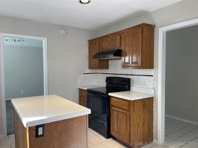 kitchen featuring a textured ceiling, black range with electric cooktop, tile countertops, a kitchen island, and light tile patterned flooring