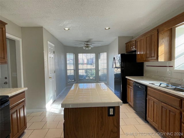 kitchen with a textured ceiling, ceiling fan, black appliances, a kitchen island, and tile counters