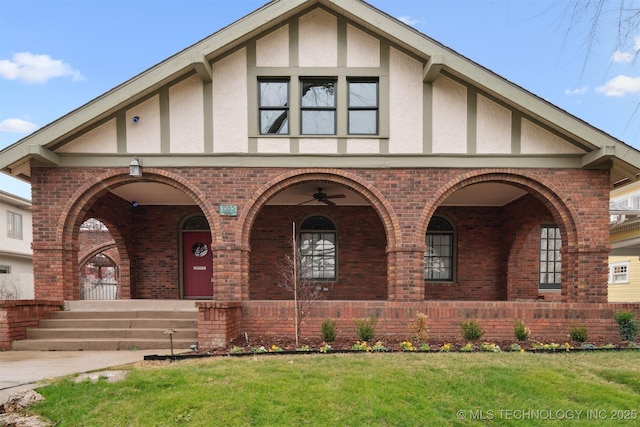 english style home with a porch, ceiling fan, and a front lawn