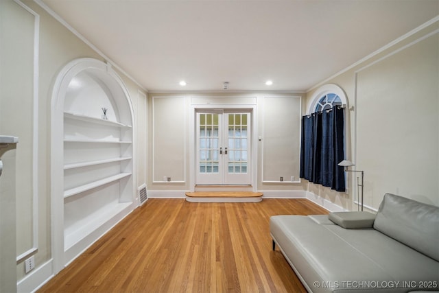 interior space with crown molding, built in features, french doors, and light wood-type flooring