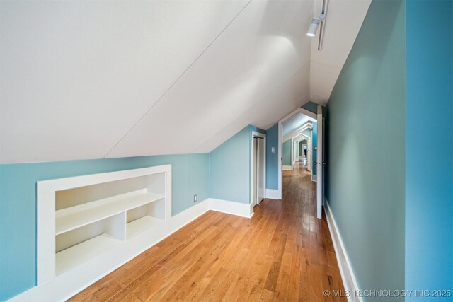 additional living space featuring lofted ceiling, light hardwood / wood-style flooring, and built in shelves