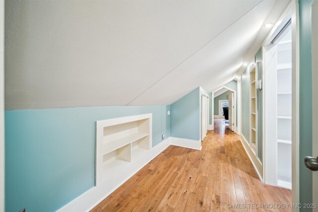 additional living space featuring lofted ceiling, light hardwood / wood-style floors, and built in shelves