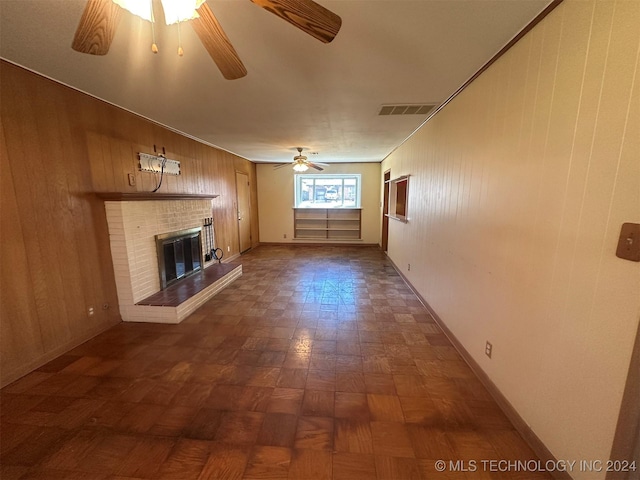 unfurnished living room featuring ceiling fan, ornamental molding, a fireplace, and wooden walls