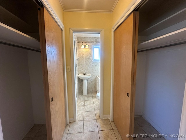 hallway with light tile patterned floors, crown molding, and tile walls