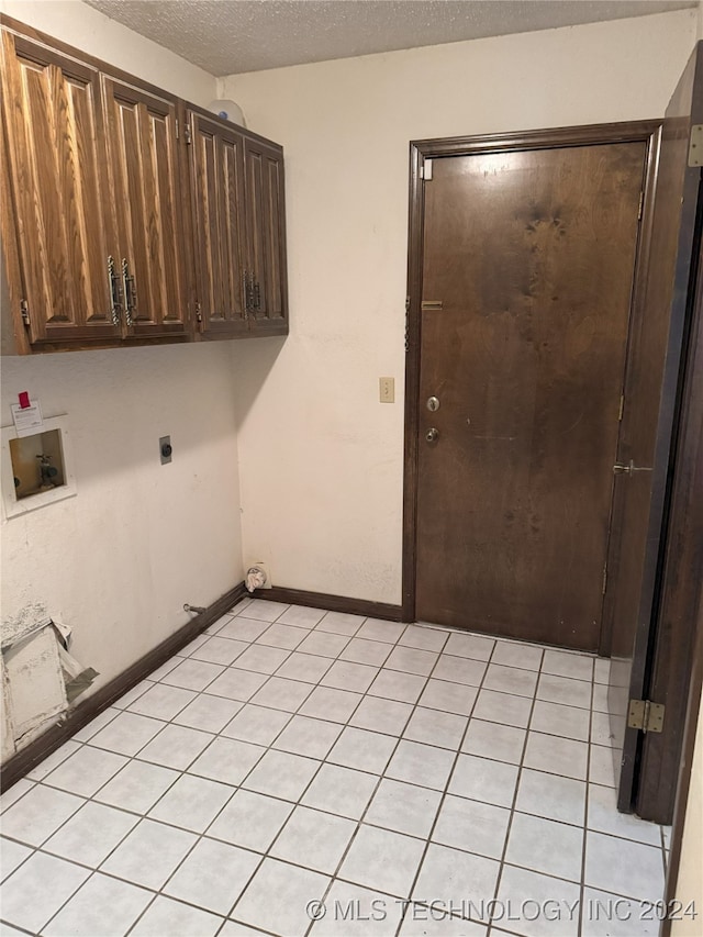 washroom with electric dryer hookup, cabinets, washer hookup, light tile patterned floors, and a textured ceiling