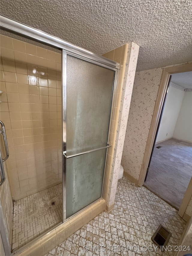 bathroom featuring toilet, a shower with shower door, and a textured ceiling