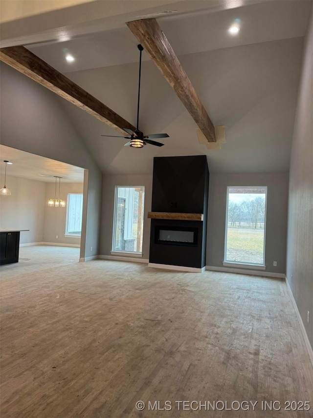 unfurnished living room with beamed ceiling, ceiling fan, a large fireplace, and light hardwood / wood-style floors