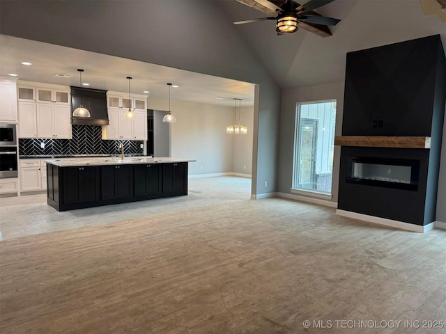 kitchen featuring premium range hood, white cabinetry, hanging light fixtures, stainless steel appliances, and an island with sink