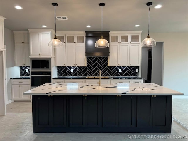 kitchen with wall oven, light stone countertops, and a large island with sink