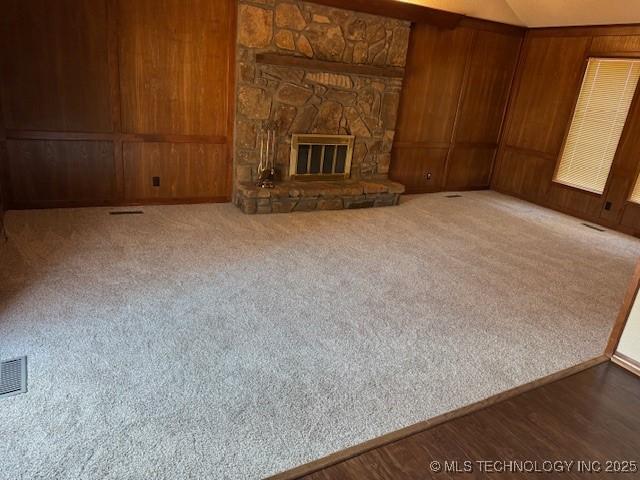 unfurnished living room featuring lofted ceiling, wood walls, a stone fireplace, and carpet floors