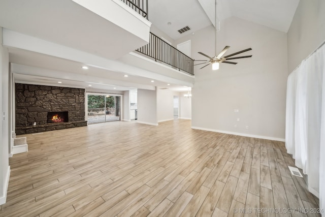 unfurnished living room featuring a stone fireplace, ceiling fan, and a towering ceiling