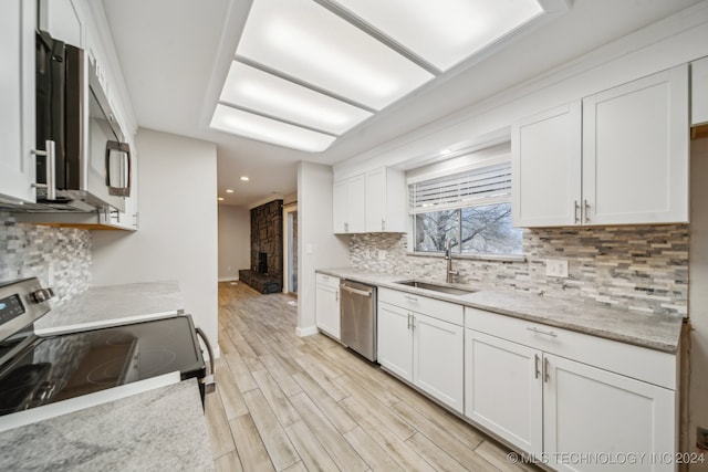 kitchen with light wood finished floors, tasteful backsplash, stainless steel appliances, white cabinetry, and a sink