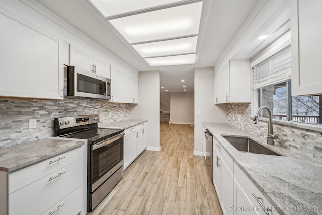 kitchen featuring white cabinets, sink, light wood-type flooring, light stone counters, and stainless steel appliances