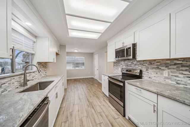 kitchen featuring white cabinets, stainless steel appliances, light stone counters, and sink