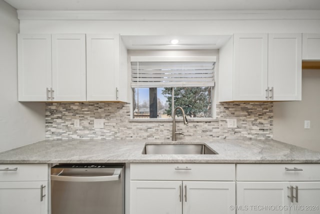 kitchen featuring light stone counters, white cabinetry, a sink, stainless steel dishwasher, and backsplash