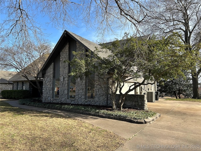 view of home's exterior with central air condition unit, stone siding, and driveway