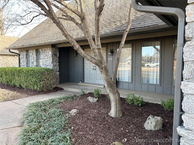 view of exterior entry featuring stone siding and roof with shingles