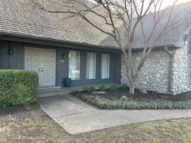 view of exterior entry with stone siding and roof with shingles