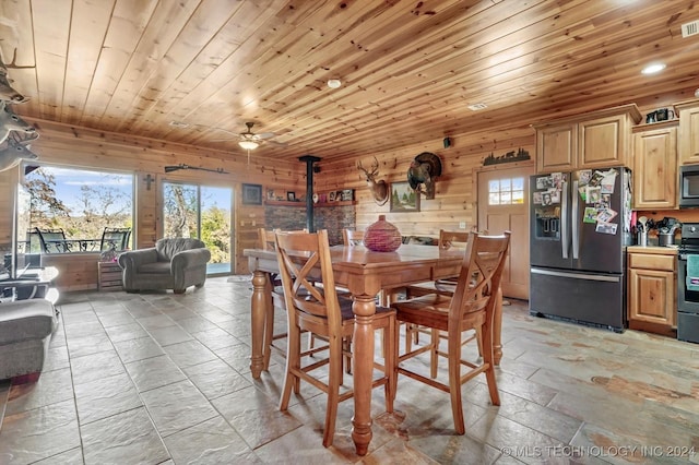 dining area with a wood stove, wood walls, ceiling fan, and wooden ceiling