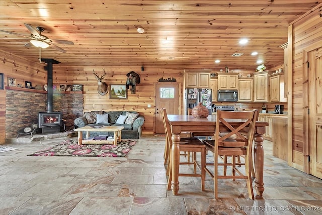 dining area with a wood stove, wood walls, ceiling fan, and wooden ceiling