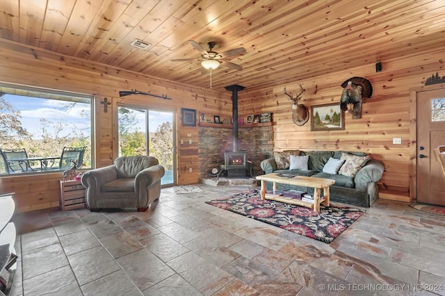 living room featuring wooden ceiling, a wood stove, ceiling fan, and wooden walls