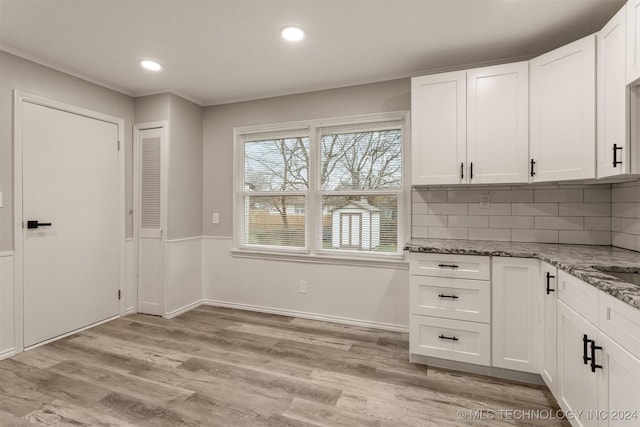 kitchen with white cabinetry, tasteful backsplash, light hardwood / wood-style flooring, dark stone counters, and ornamental molding