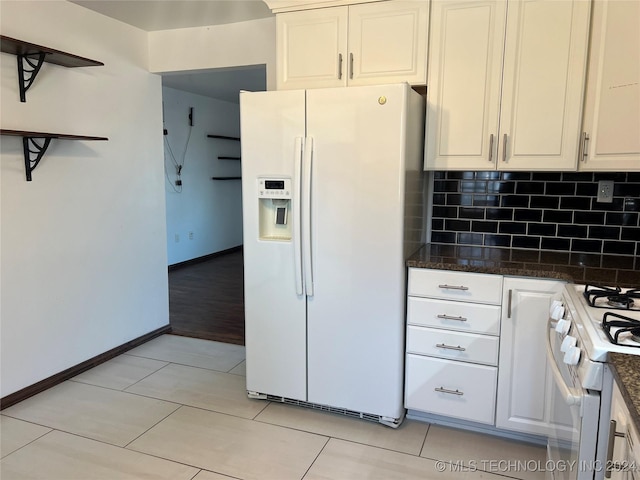 kitchen with white cabinets, dark stone countertops, white appliances, decorative backsplash, and light tile patterned floors