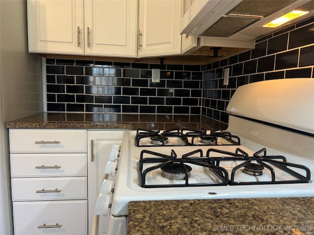 interior details featuring white gas range, backsplash, dark stone countertops, white cabinets, and exhaust hood