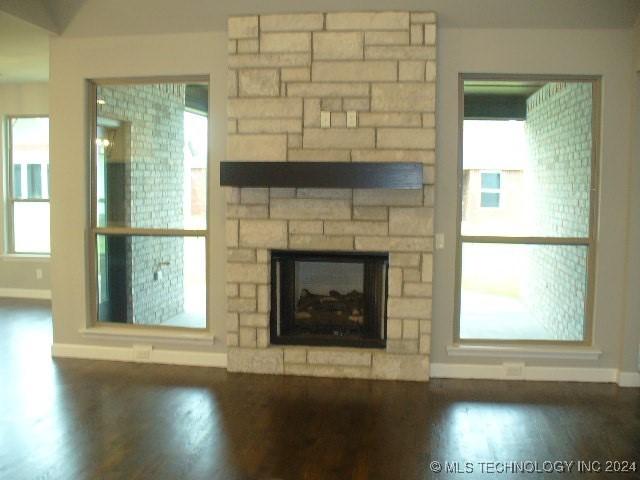 unfurnished living room featuring a stone fireplace and dark hardwood / wood-style flooring