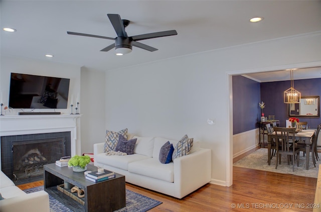 living room with a tile fireplace, crown molding, hardwood / wood-style floors, and ceiling fan with notable chandelier