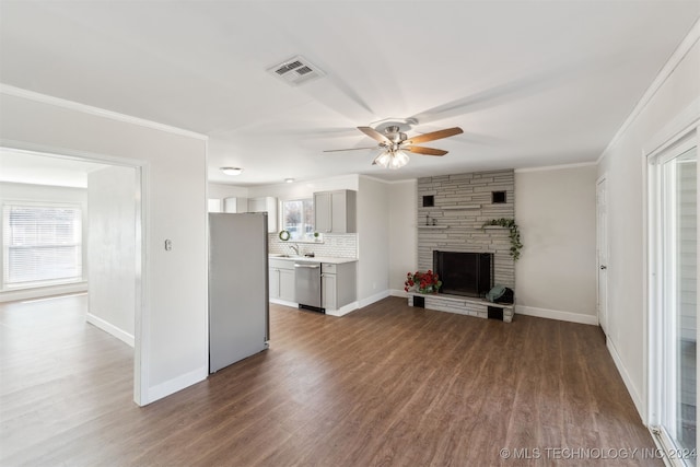 unfurnished living room with ceiling fan, sink, a stone fireplace, dark hardwood / wood-style floors, and ornamental molding