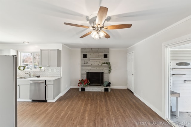 unfurnished living room with ceiling fan, sink, light hardwood / wood-style floors, a fireplace, and ornamental molding