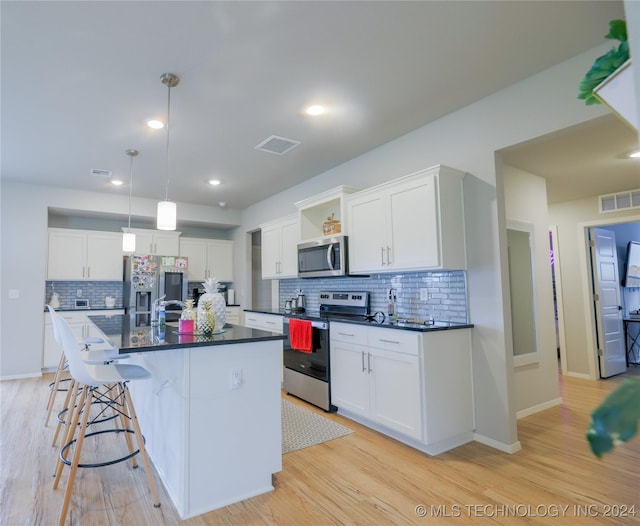 kitchen with an island with sink, white cabinets, pendant lighting, and appliances with stainless steel finishes