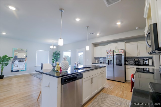 kitchen with sink, an island with sink, appliances with stainless steel finishes, decorative light fixtures, and white cabinetry