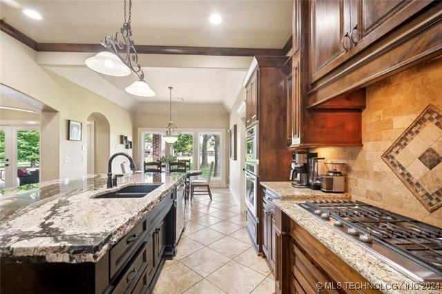 kitchen featuring backsplash, a kitchen island with sink, sink, light stone countertops, and stainless steel appliances