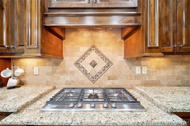 kitchen with light stone countertops, backsplash, and stainless steel gas cooktop