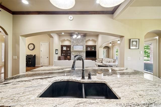 kitchen with a stone fireplace, light stone countertops, sink, and an inviting chandelier