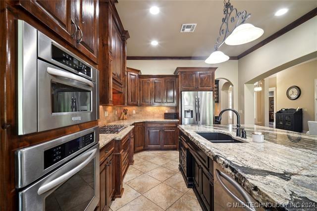 kitchen with light stone countertops, sink, stainless steel appliances, tasteful backsplash, and pendant lighting