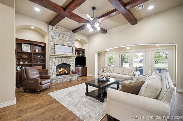 living room with coffered ceiling, beam ceiling, built in features, hardwood / wood-style floors, and a stone fireplace