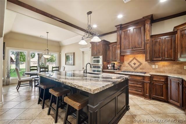 kitchen with a center island with sink, hanging light fixtures, decorative backsplash, light stone countertops, and a breakfast bar area