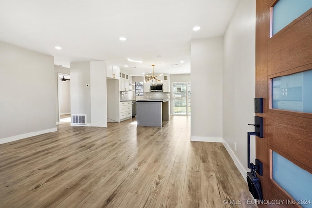 unfurnished living room with an inviting chandelier and light hardwood / wood-style flooring