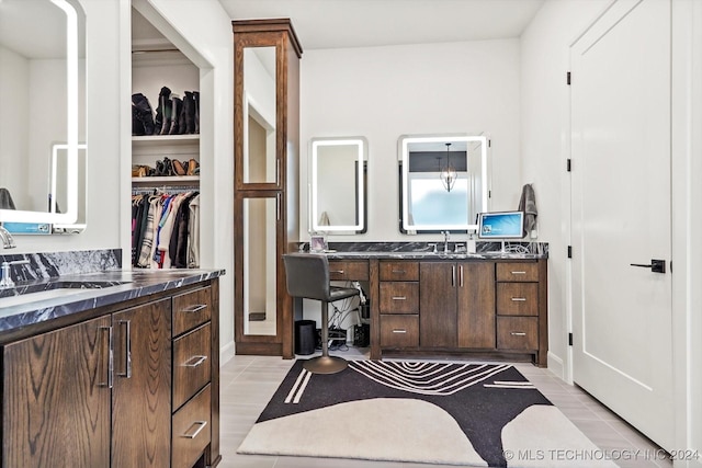 bathroom with a walk in closet, two vanities, a sink, and tile patterned floors