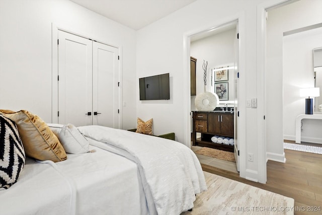 bedroom with a closet, light wood-type flooring, ensuite bath, and baseboards