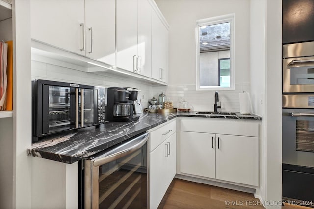 kitchen with beverage cooler, backsplash, a sink, and white cabinetry