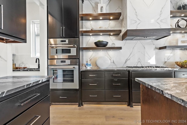 kitchen with light stone counters, range hood, open shelves, stainless steel appliances, and tasteful backsplash